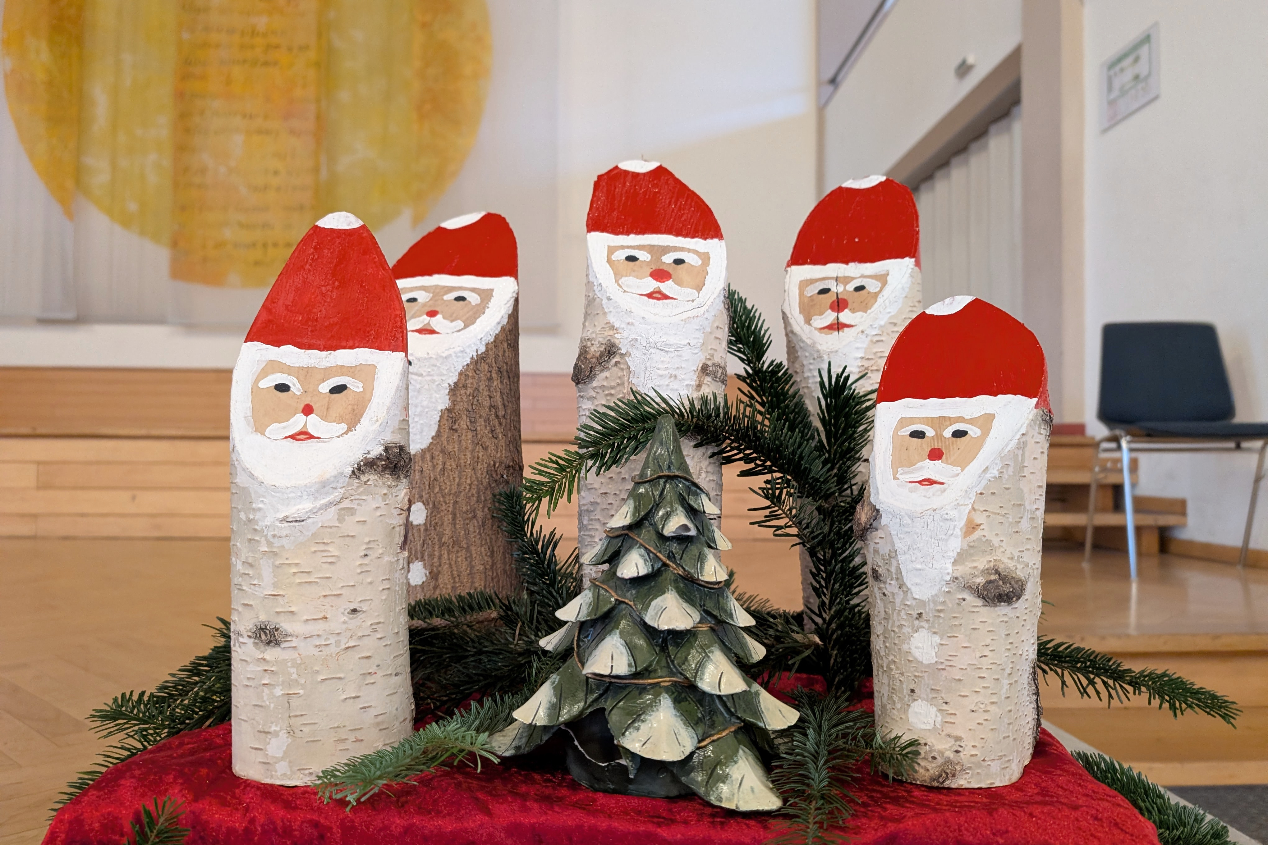 Vorweihnachtlicher Nachmittag Fünf aus Baumstämmen gebastelte Nikoläuse stehen um einen kleinen Dekotannenbaum.