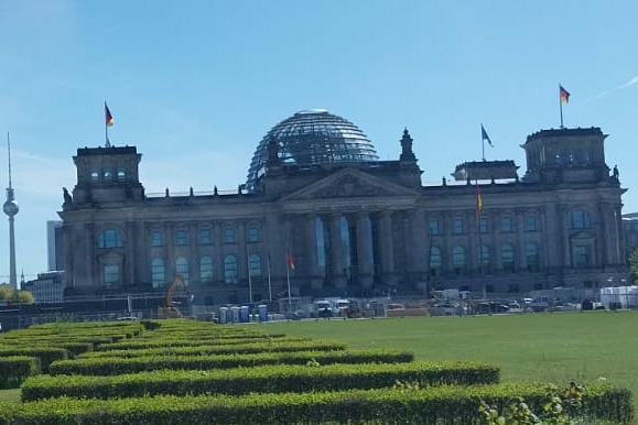 Das Reichstagsgeb&auml;ude mit drei wehenden Fahnen und gr&uuml;nen Hecken im Vordergrund