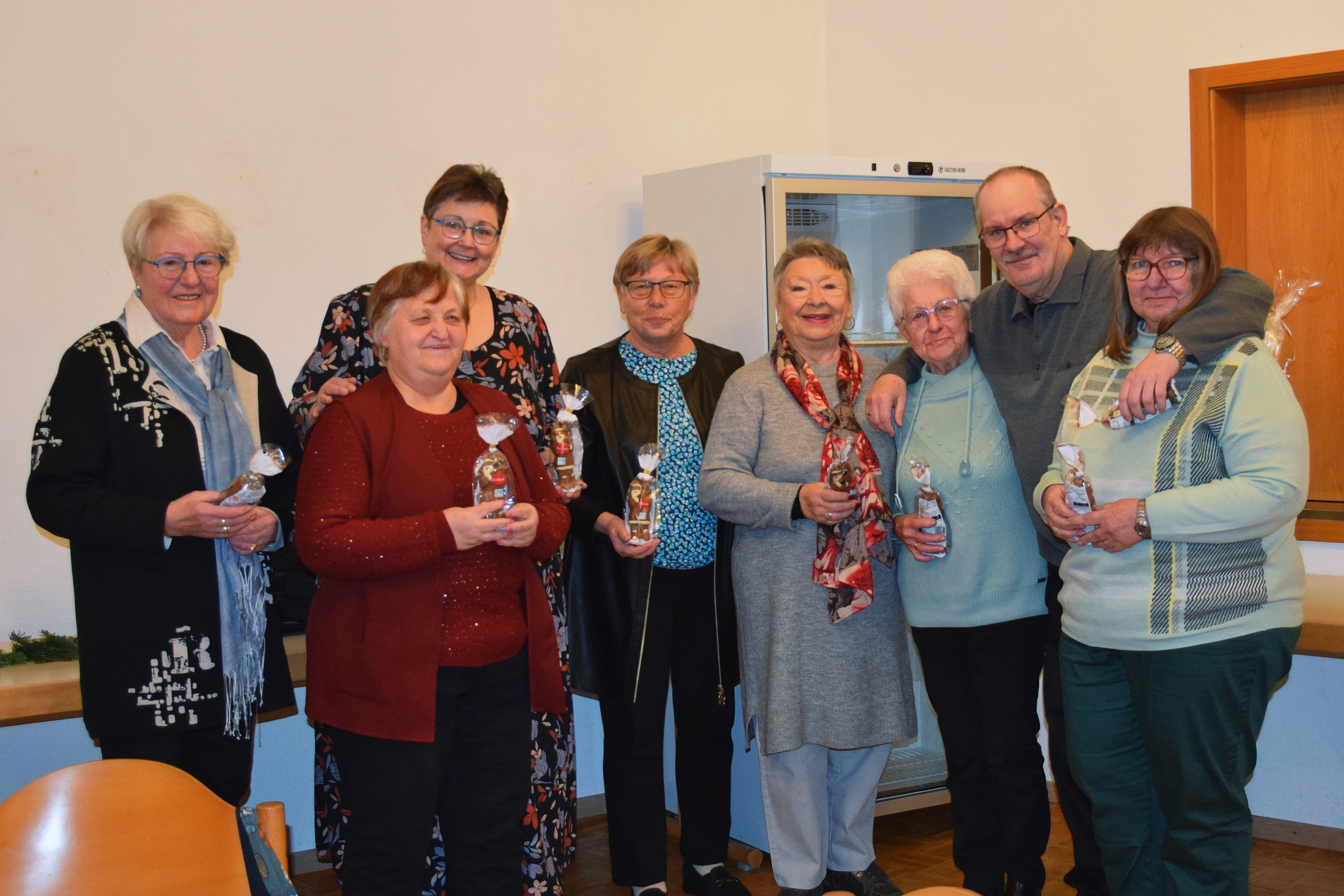 Gruppenbild mit sieben Frauen unterschiedlichen Alters und einem Mann, die nebeneinander stehen und kleine Geschenkt&uuml;ten in den H&auml;nden halten.