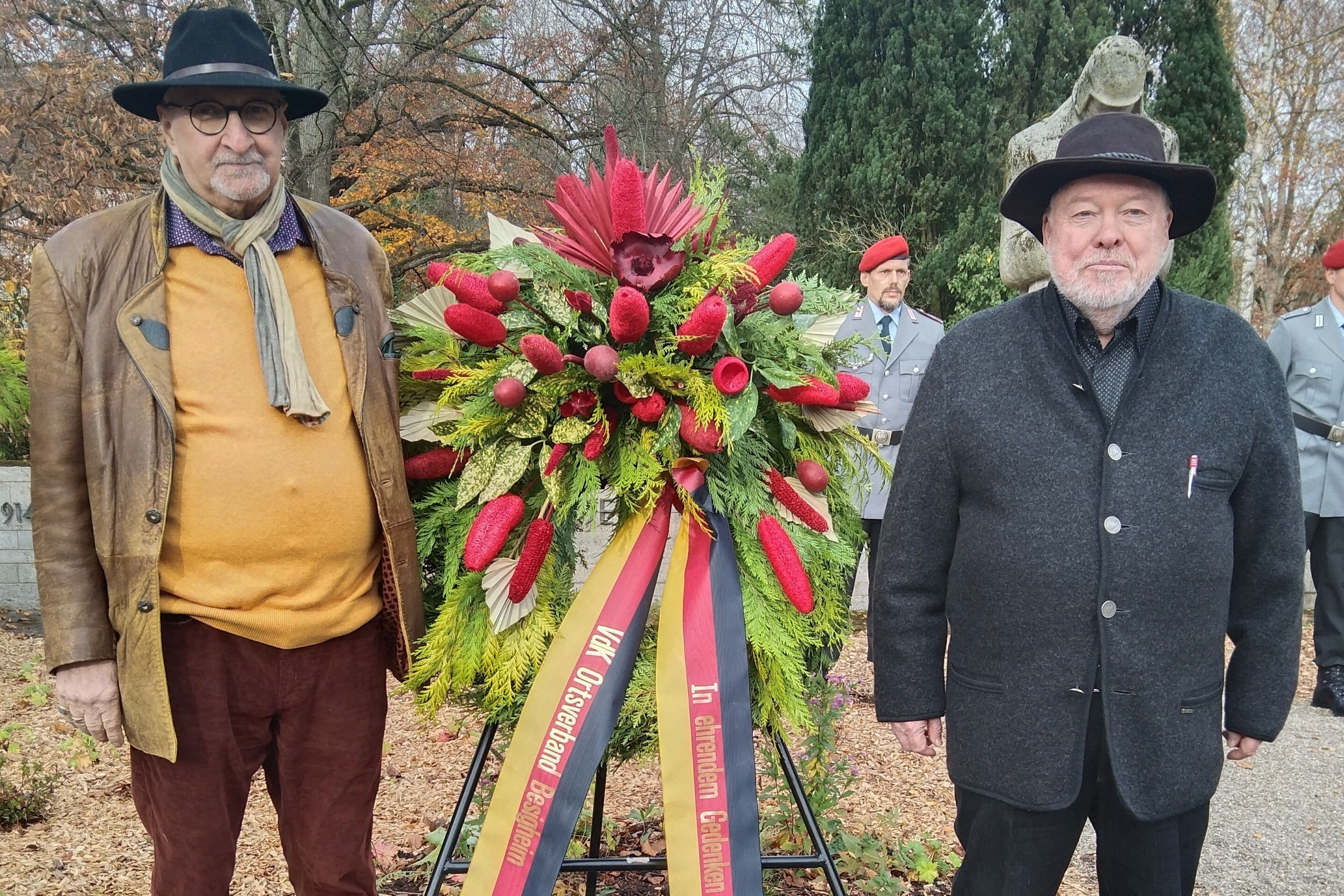 Benno Belzhuber und Karl Reichert stehen neben einem Kranzgebinde vor einem Ehrenmal