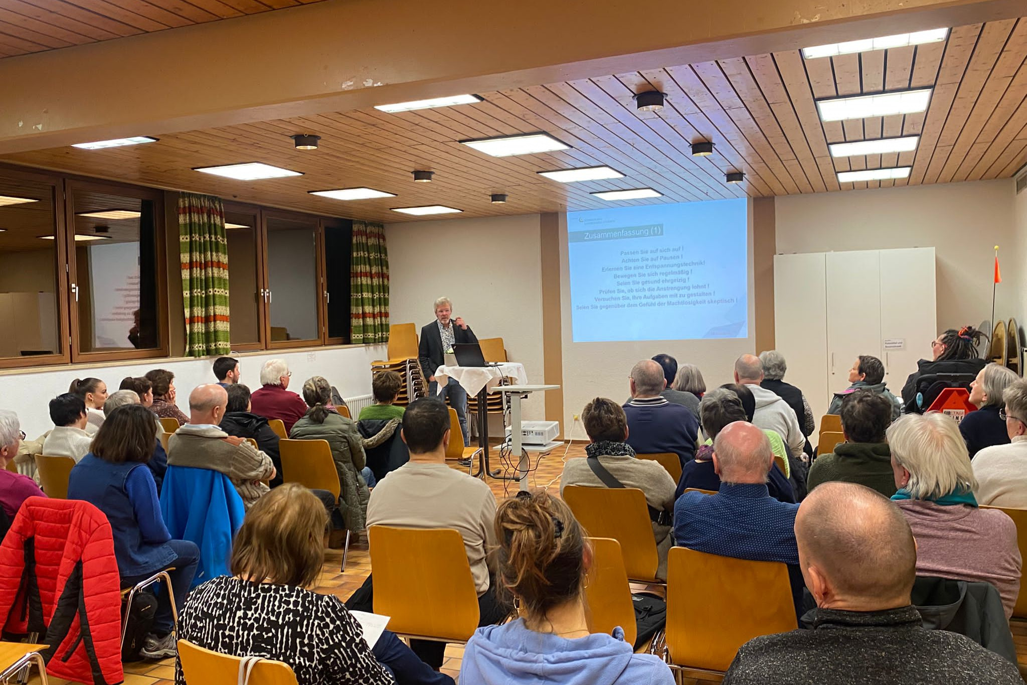 Gute Resonanz auf Vortrag "Mentale Gesundheit schützen" im Pfarrsaal in Schönau im Schwarzwald Rückenansicht sitzender Besuchende im Pfarrsaal Schönau beim Vortrag von Dr. Thomas Unterbrink (vorne)