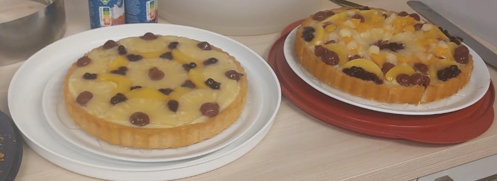 Zwei vollständige Kuchen stehen nebeneinander. Sie sind mit verschiedenen Obstsorten belegt.