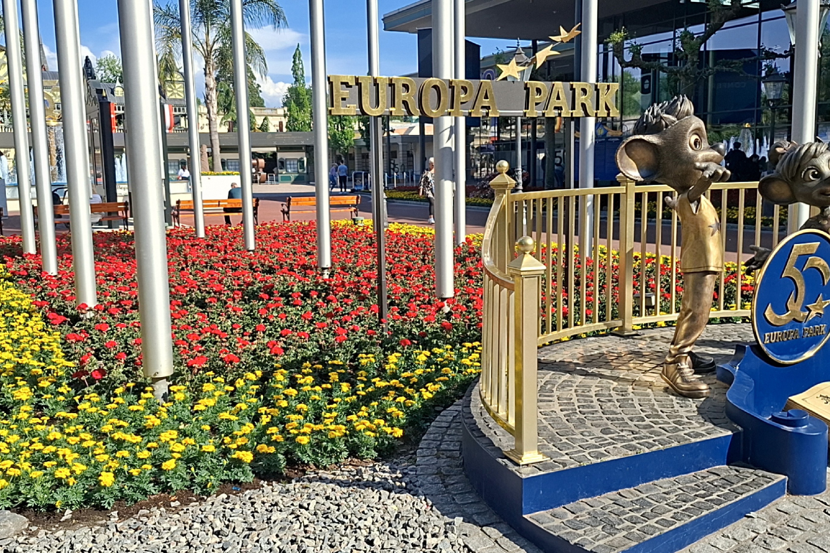 Das Bild zeigt den Eingangsbereicht des Europa Parks. Zu sehen sind die Maskottchen und der Schriftzug vor einem Feld von Blumen.